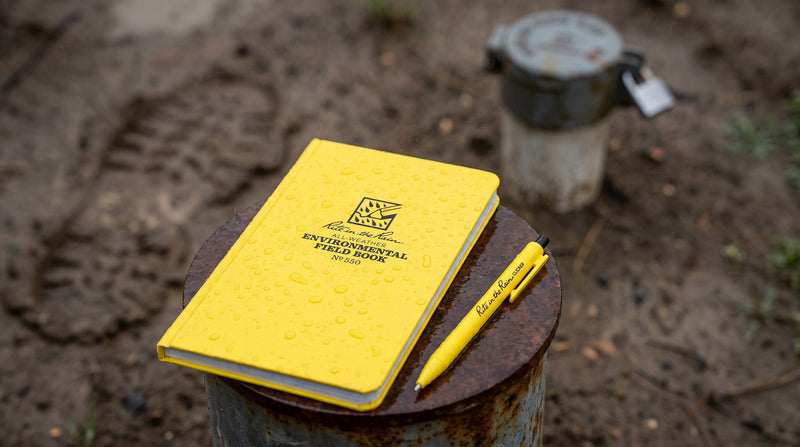 Carnet de terrain environnemental jaune Rite in the Rain et stylo sur un tubage de puits rouillé sous la pluie