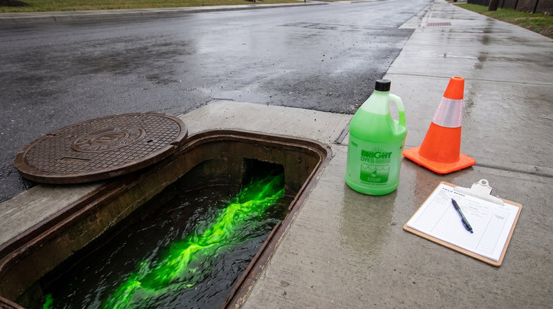 Fluorescent tracer dye container beside an open manhole with dyed flow visible during a sewer dye test