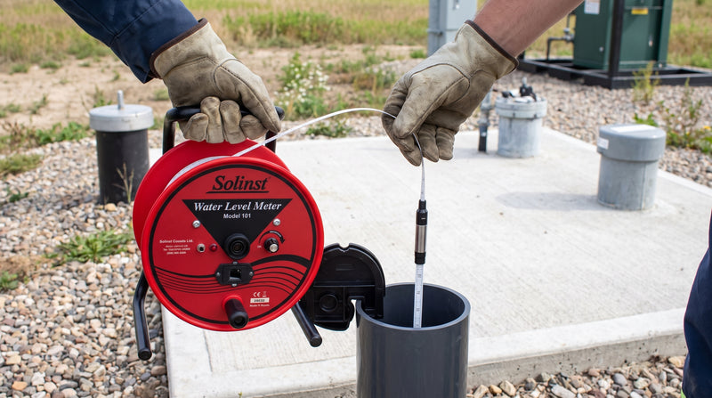 Environmental consultant lowering a Solinst water level meter probe into a groundwater monitoring well